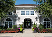 Thumbnail 51 of 53 - A white building with a black door and windows surrounded by plants.