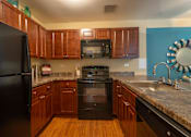 Thumbnail 24 of 31 - A black refrigerator is in a kitchen with wooden cabinets.
