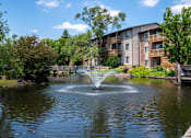 Thumbnail 8 of 31 - A fountain in the middle of a pond in front of apartment buildings.