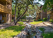 Thumbnail 7 of 31 - A stream runs through a grassy area between two apartment buildings.
