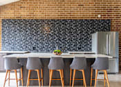 Thumbnail 54 of 62 - A kitchen with a brick wall and a bar area with grey chairs.