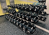 Thumbnail 35 of 62 - A row of black dumbbells are lined up on a rack in a gym.