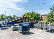 Thumbnail 23 of 62 - A wooden deck with blue couches and a table with chairs.