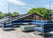 Thumbnail 24 of 62 - A wooden deck with blue couches and a table.