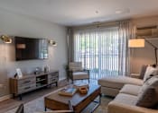Thumbnail 5 of 43 - A well-lit living room with a wooden coffee table and a large window with curtains.