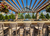 Thumbnail 29 of 73 - A patio with a bar and chairs under a wooden pergola.