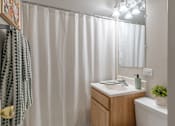 Thumbnail 8 of 25 - A bathroom with a white shower curtain, a wooden vanity, and a small potted plant.