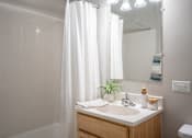 Thumbnail 9 of 25 - A bathroom with a white shower curtain, a wooden vanity, and a mirror.