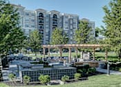 Thumbnail 46 of 53 - A large building with a lot of windows is behind a landscaped area with a fountain.