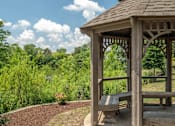 Thumbnail 14 of 23 - A wooden gazebo with a bench is situated in a garden.