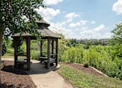 Thumbnail 16 of 23 - A gazebo with a bench is surrounded by greenery.