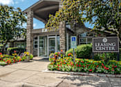 Thumbnail 6 of 23 - A leasing center is surrounded by flowers and has a handicap parking sign.