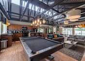 Thumbnail 34 of 44 - A pool table is in the middle of a room with a kitchen in the background.