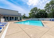 Thumbnail 16 of 44 - A large outdoor swimming pool with lounge chairs and a building in the background.