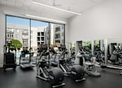 Thumbnail 13 of 18 - A gym with a view of apartment buildings outside the large windows.