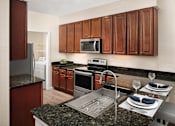 Thumbnail 4 of 18 - A kitchen with brown cabinets and a granite countertop.
