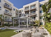 Thumbnail 9 of 19 - A modern apartment complex with a communal outdoor area featuring a table and chairs.