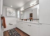 Thumbnail 14 of 18 - A bathroom with white cabinets and a brown rug.
