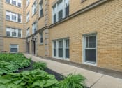 Thumbnail 3 of 18 - a brick apartment building with a sidewalk and plants in front of it