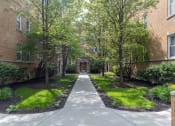 Thumbnail 1 of 22 - a walkway with trees and grass in front of an apartment building