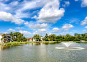 Thumbnail 45 of 51 - A fountain in the middle of a lake with buildings and trees in the background.