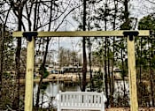 Thumbnail 48 of 49 - A white bench is situated under a wooden structure in a wooded area.