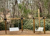Thumbnail 49 of 49 - Two wooden swing sets in a field with trees in the background.