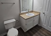 Thumbnail 40 of 49 - A bathroom with a toilet, sink, mirror, and wooden floors.