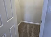 Thumbnail 42 of 49 - A white door is on the left of a hallway with a carpeted floor and a wire shelf on the wall.