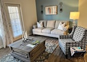 Thumbnail 22 of 33 - A living room with a grey couch, a patterned chair, and a coffee table.