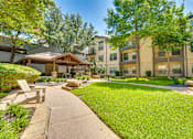 Thumbnail 63 of 69 - A sunny day at a well-kept apartment complex with a grassy area and a wooden bench.