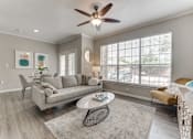 Thumbnail 1 of 81 - A living room with a grey couch, a round table, and a ceiling fan. at The Brazos, Dallas