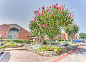 Thumbnail 40 of 42 - A red flowering tree in front of a brick building at Copper Hill Apartments, Bedford