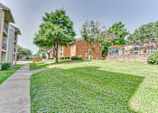Thumbnail 31 of 42 - A grassy area with a sidewalk and a building in the background at Copper Hill Apartments, Bedford, Texas