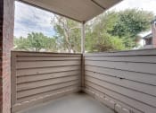 Thumbnail 12 of 57 - a covered porch with a view of trees and a brick house at Indian Creek Apartments, Carrollton, 75007