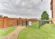 Thumbnail 54 of 68 - A black metal fence surrounds a grassy area with a brick wall on one side and a dirt path leading to a gate at Limestone Ranch Apartments, Lewisville 75067