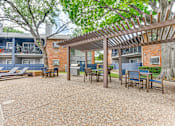 Thumbnail 25 of 51 - A patio with a pergola and chairs is surrounded by apartment buildings. at The Manhattan Apartments, Dallas, Texas