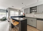 Thumbnail 38 of 51 - A kitchen with a black countertop and wooden chairs. at The Manhattan Apartments, Dallas, TX