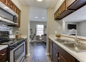 Thumbnail 12 of 51 - A kitchen with a black stove top oven and wooden cabinets. at The Manhattan Apartments, Dallas, 75252