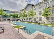 Thumbnail 38 of 52 - Courtyard pool with sunbathing areas and greenery at The Montrose Apartments, Dallas, Texas