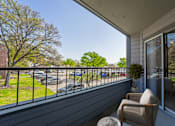 Thumbnail 13 of 41 - A balcony with a chair and a potted plant overlooking a parking lot.