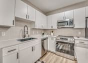 Thumbnail 3 of 53 - Modern kitchen with white cabinets and stainless appliances at The Barton Apartments, Dallas