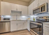 Thumbnail 10 of 29 - A kitchen with white cabinets and stainless steel appliances.