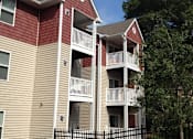 Thumbnail 2 of 7 - A red and beige apartment building with a black fence in front.