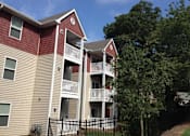 Thumbnail 3 of 7 - A red and beige apartment building with a black fence in front.