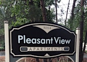 Thumbnail 4 of 13 - A sign for Pleasant View Apartments is shown in front of a wooded area.