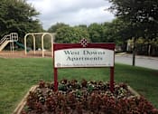 Thumbnail 4 of 9 - A sign for West Downs Apartments sits in a flower bed.