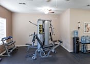 Thumbnail 15 of 22 - A home gym with a weight machine, a bench, and a water cooler.