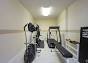 Thumbnail 21 of 25 - A gym room with a rowing machine, a bench, and a dumbbell rack.