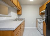 Thumbnail 12 of 25 - A kitchen with a black refrigerator, white sink, and wooden cabinets.